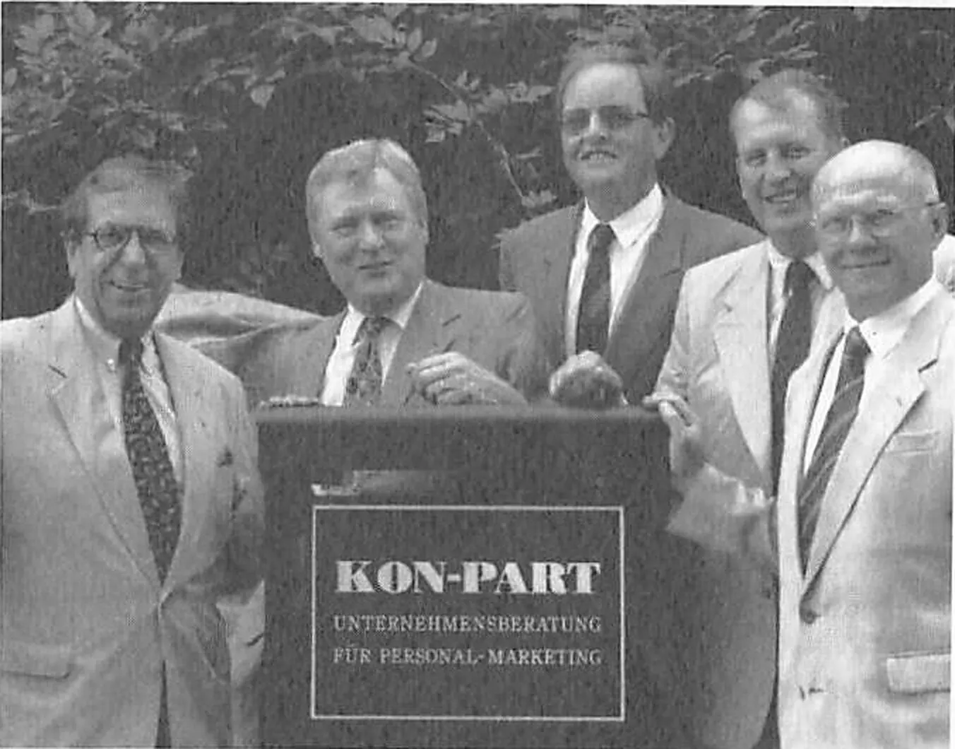 Fünf KON-PART-Partner hinter einem Schild mit der Aufschrift KON-PART Unternehmensberatung für Personal-Marketing, 1995